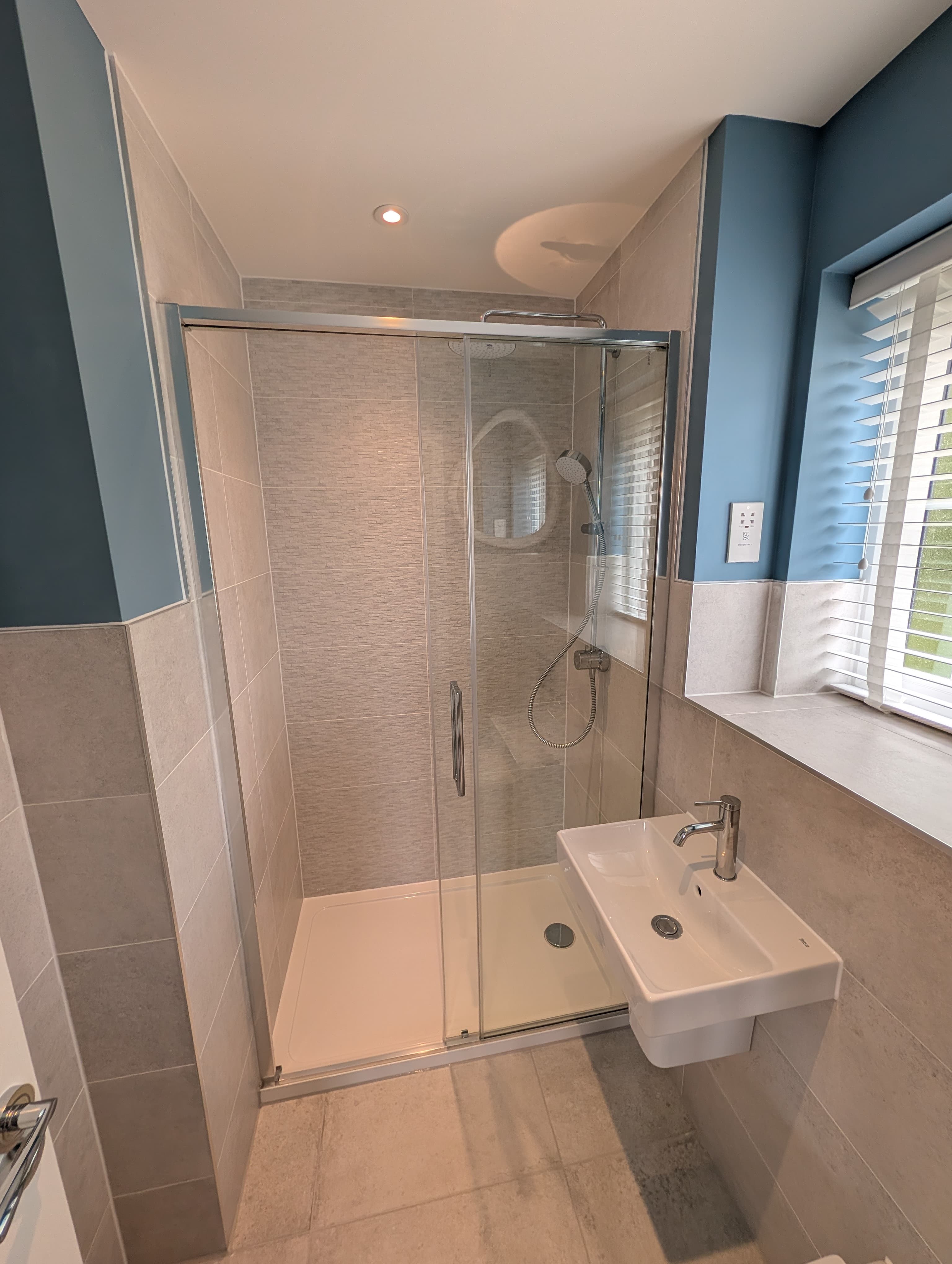 Glass shower enclosure against a blue accent wall, with round mirror reflection and wall-hung basin alongside