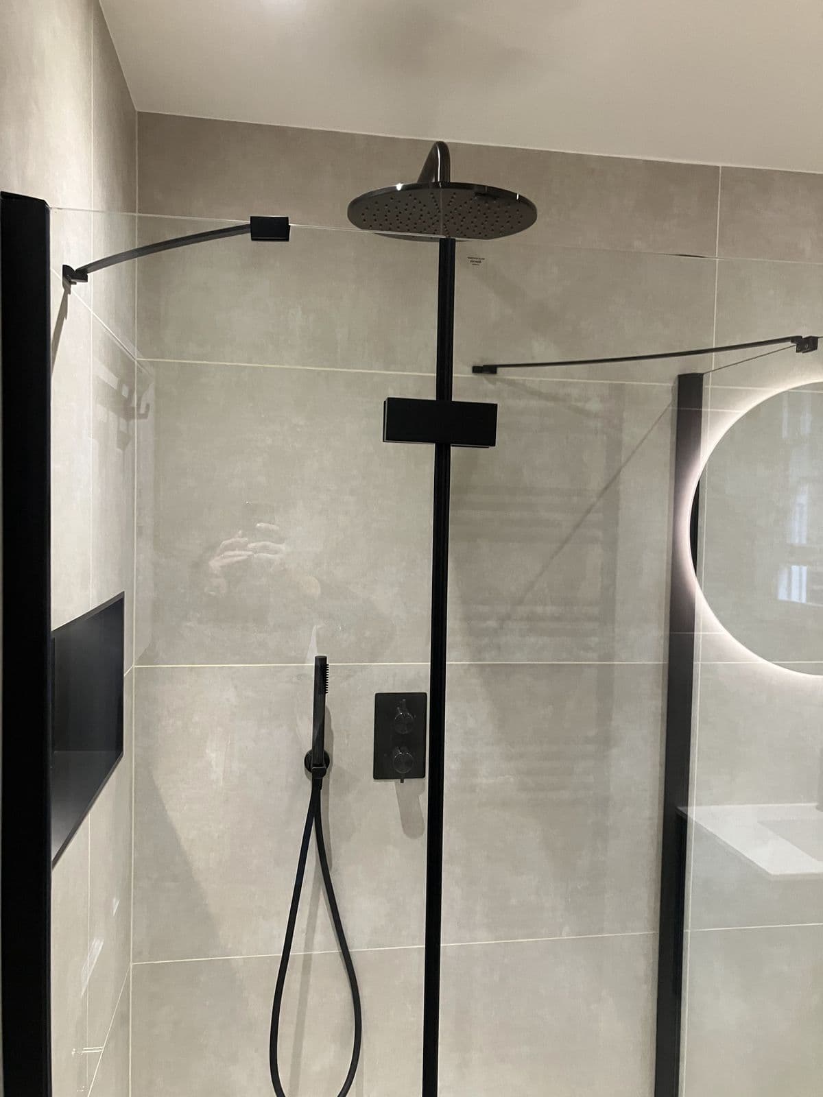 Black matt shower riser rail with overhead rainfall head and concealed thermostatic valve behind a frameless glass screen