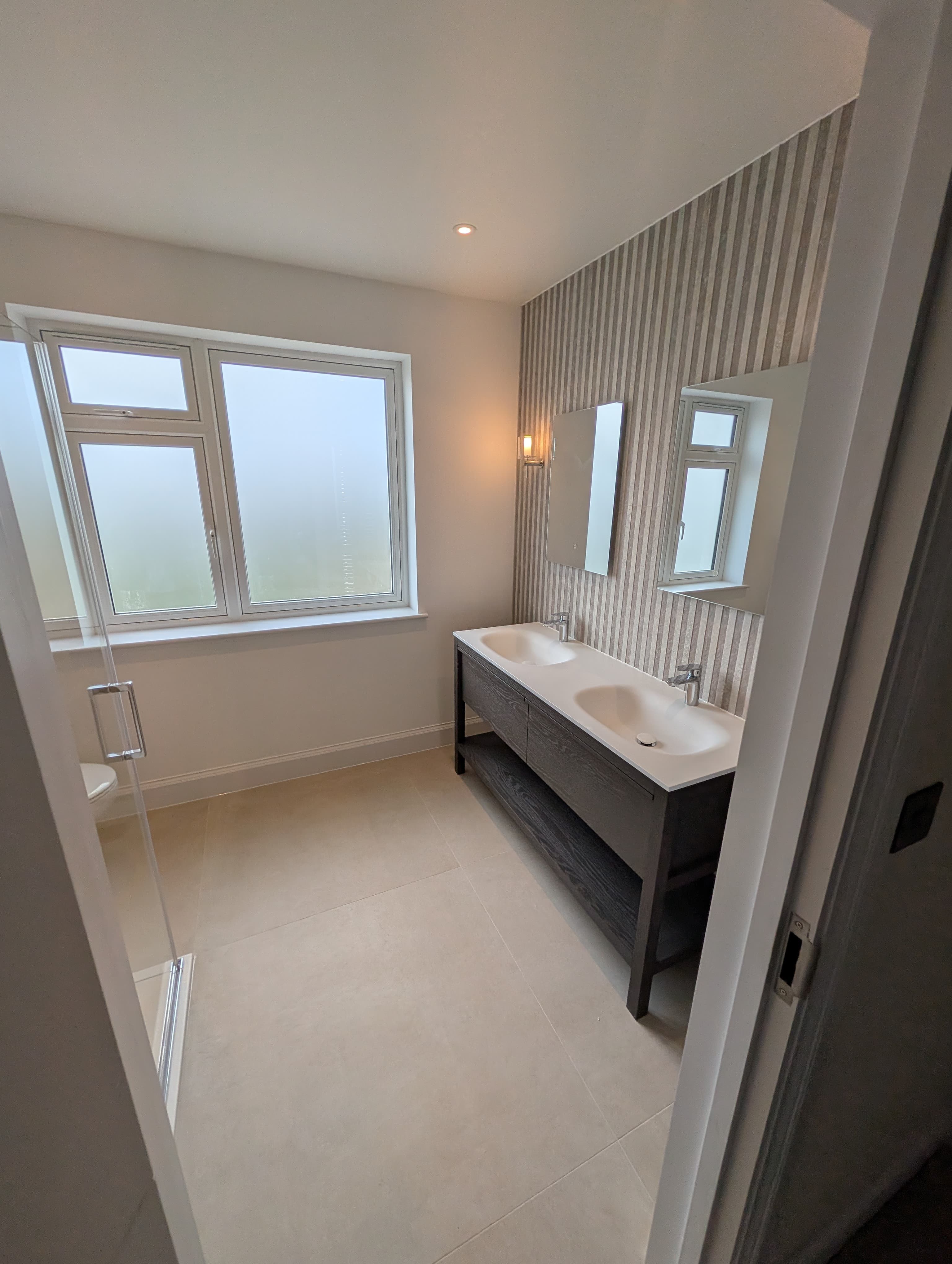 Bright en-suite bathroom with a tall window, corner glass shower screen and tiled flooring
