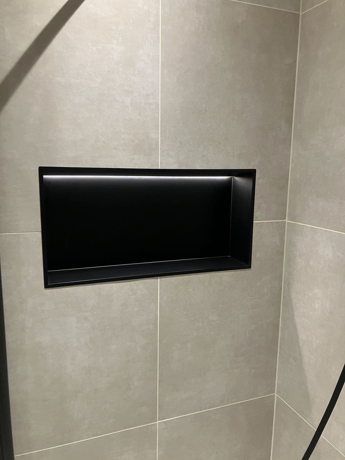 Recessed black tiled shower niche with integrated LED strip lighting, set into a stone-effect tiled wall