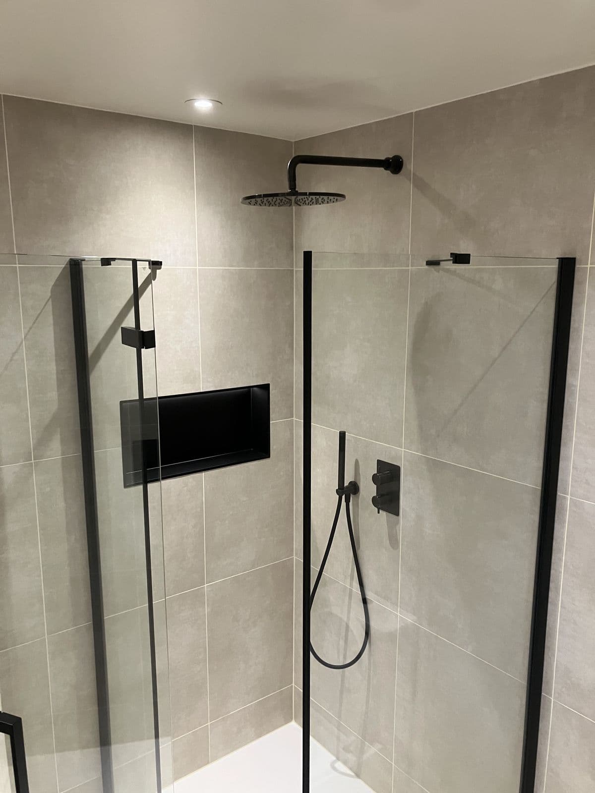 Black recessed shower niche with LED lighting, black hinged glass door and chrome pull handle