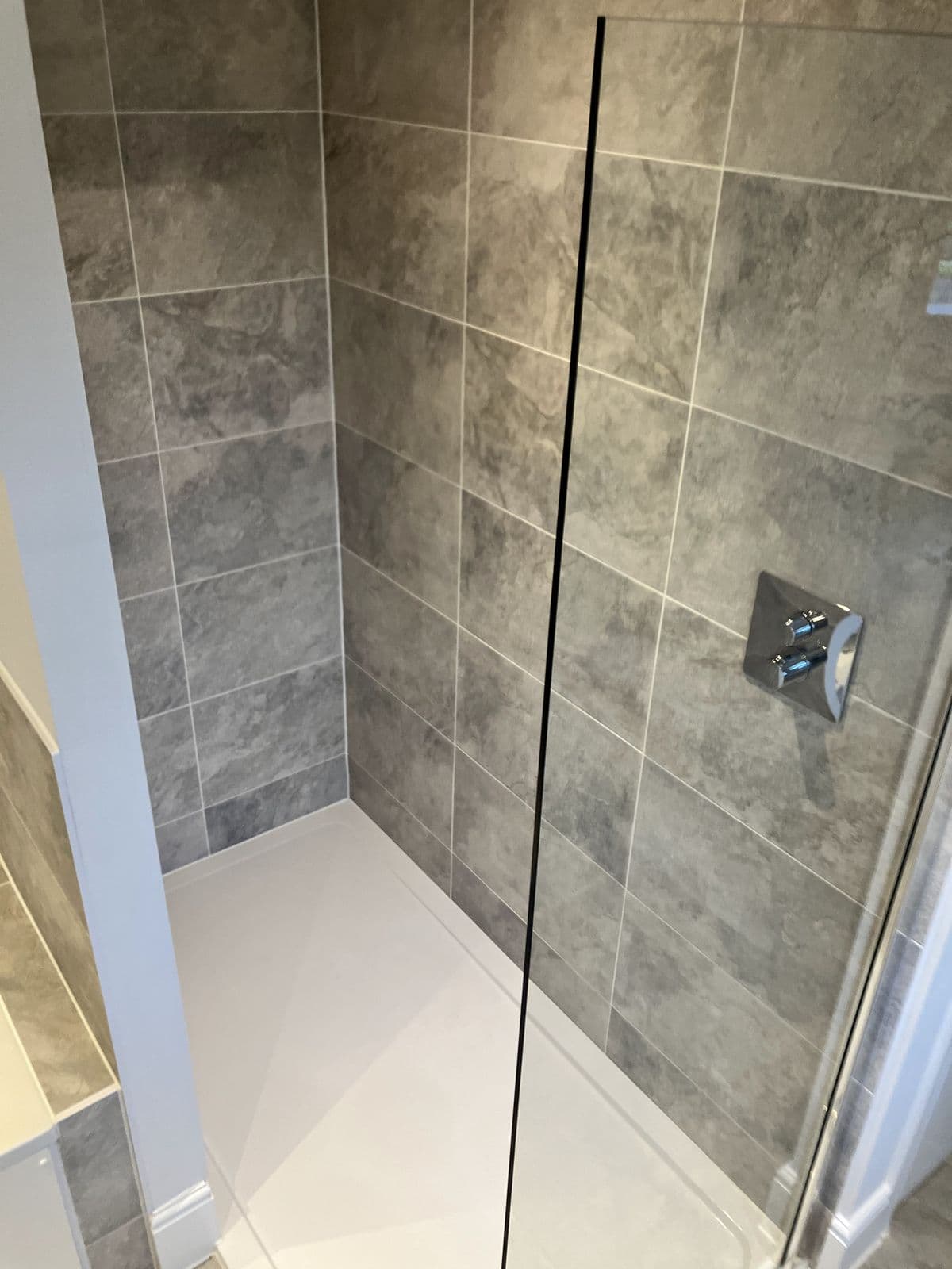 Walk-in shower with ceiling-mounted rainfall head, stone-effect tiling and chrome ladder towel rail beside a frosted window