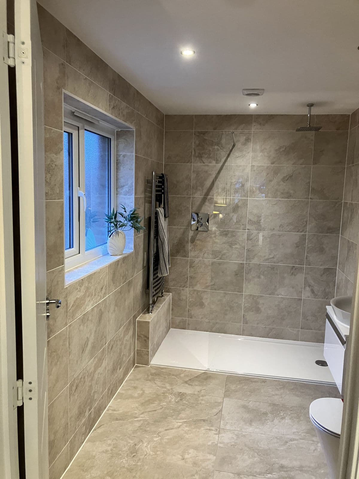 Walk-in wet-room shower with ceiling-mounted rain head, a window with plant on the sill and a chrome heated towel rail