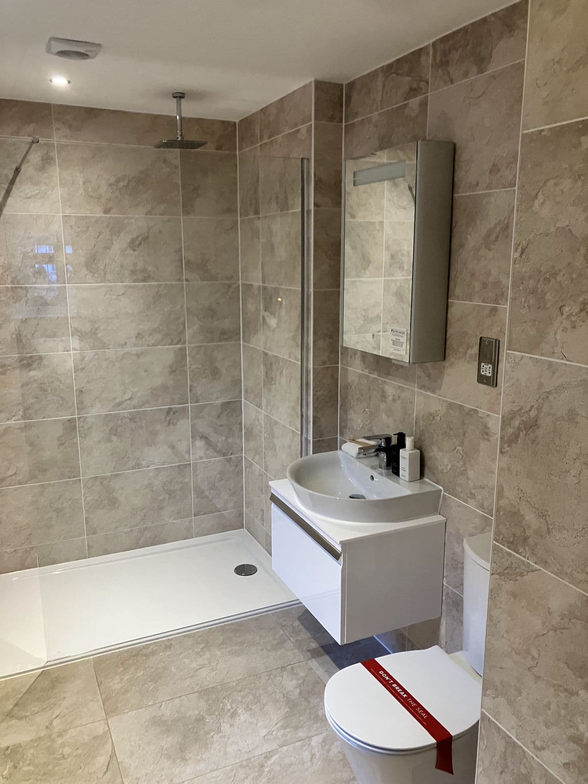 Walk-in shower with mirrored cabinet and wall-hung vanity basin, toilet still fitted with protective seal tape ready for handover