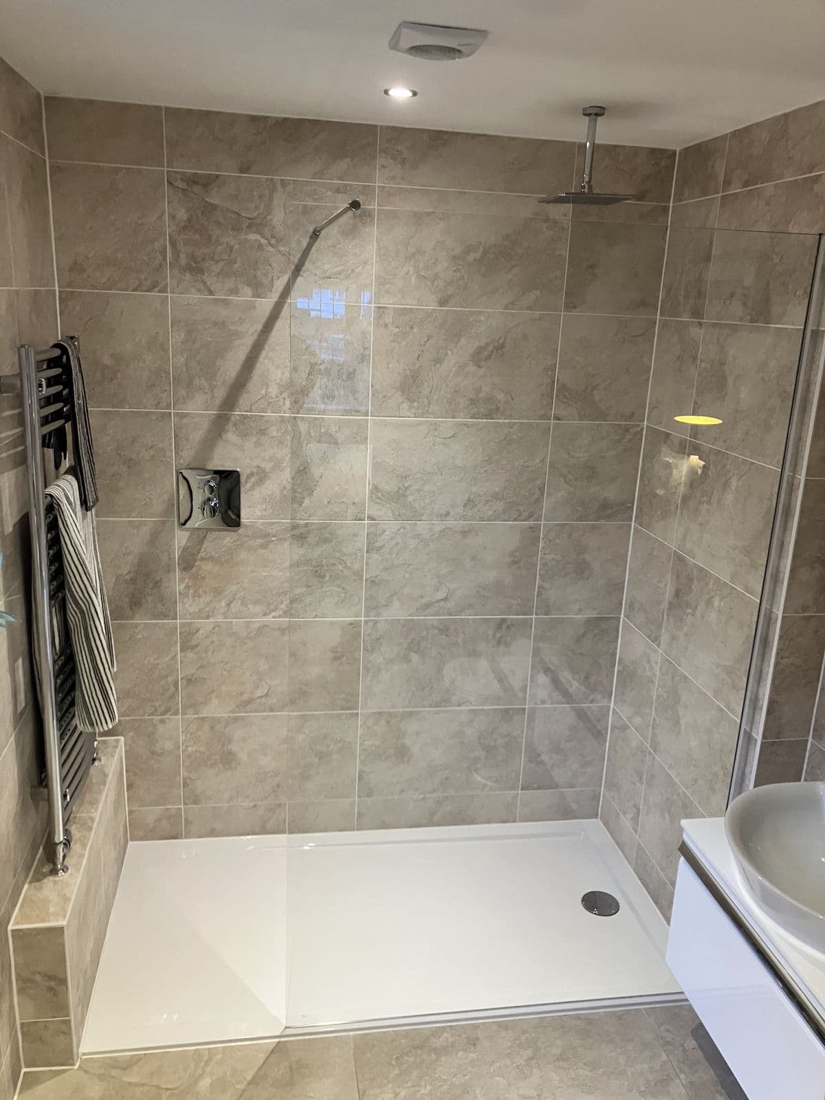 Walk-in wet-room shower with stone-effect tiling, ceiling-mounted rainfall head and chrome heated towel rail with striped towels