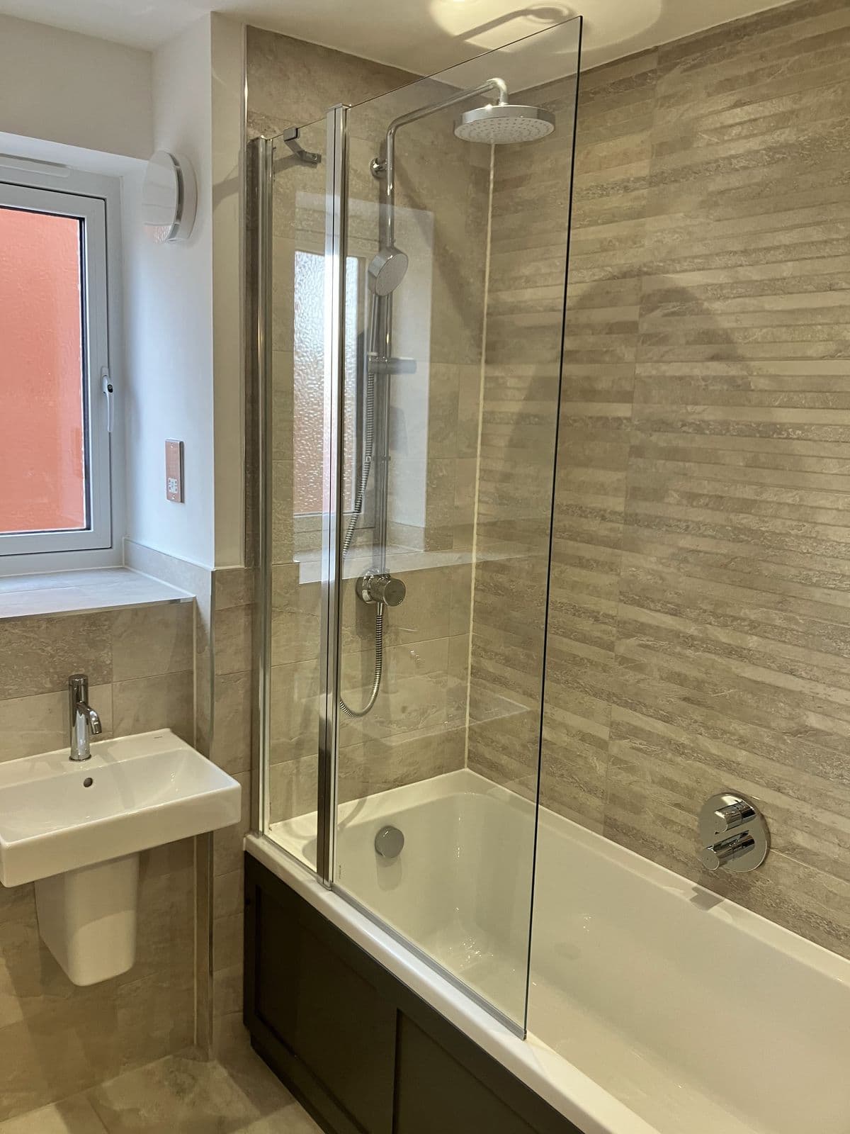 Bath with folding glass shower screen, riser-rail shower and linear stone-effect tiled feature wall