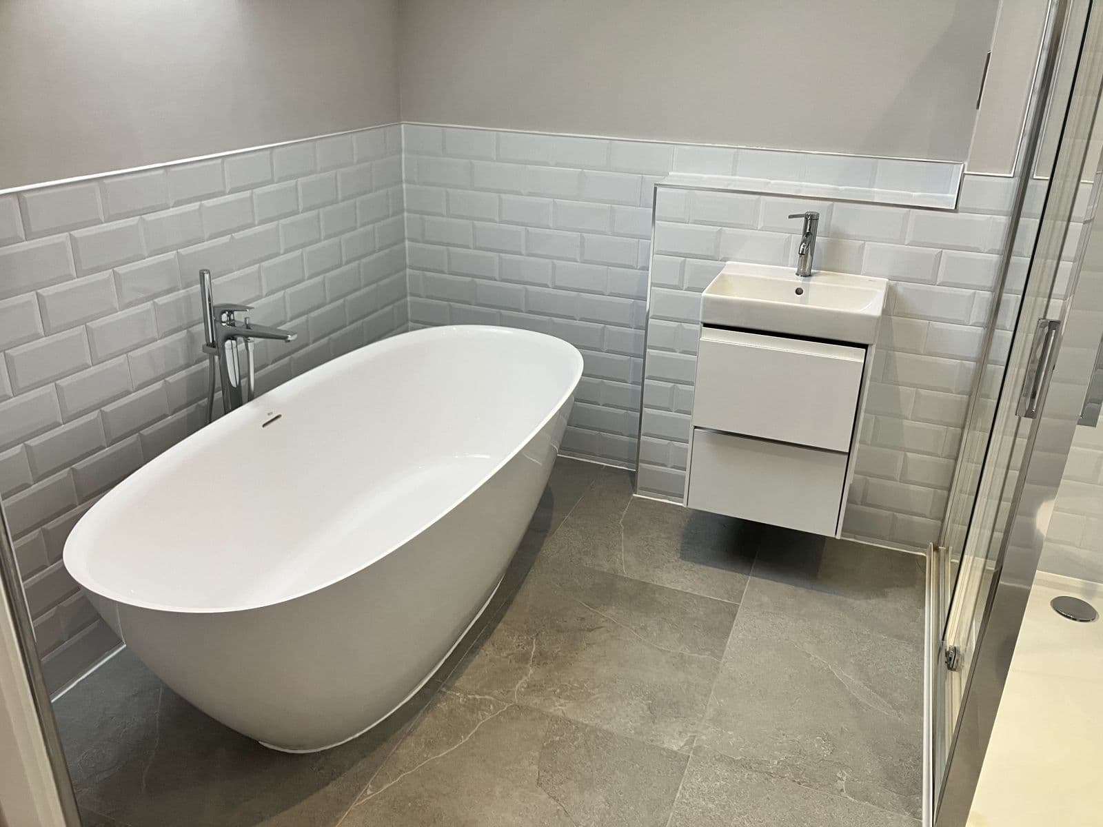 Freestanding oval bath with floor-standing chrome mixer tap against grey metro-tiled walls