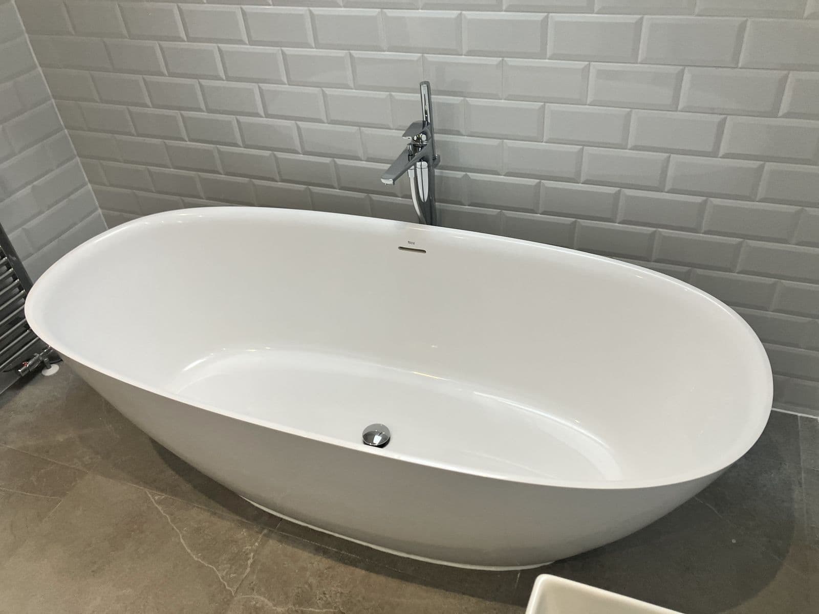 Freestanding oval bath with floor-standing chrome mixer tap and overflow, close-up against metro-tiled walls