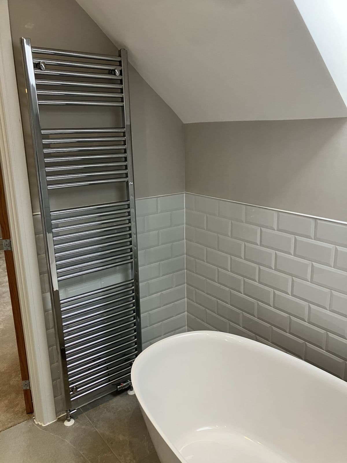 Chrome ladder heated towel rail against a sloped ceiling, beside a freestanding bath in a loft en-suite