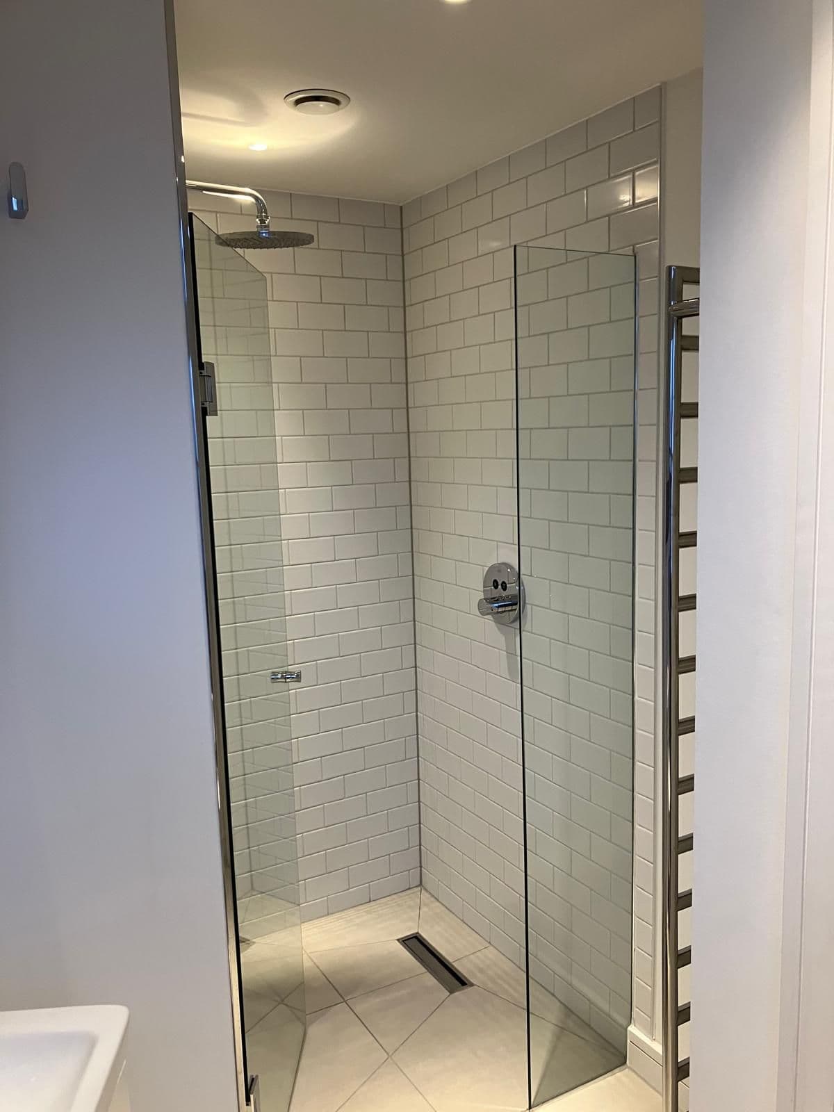 Frameless glass shower enclosure with white metro-tiled walls, rainfall shower head and chrome heated towel rail