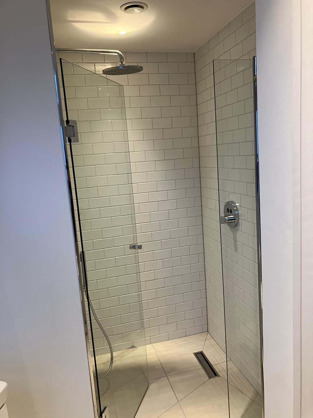White metro-tiled shower enclosure with rainfall head, hinged glass door and concealed shower valve