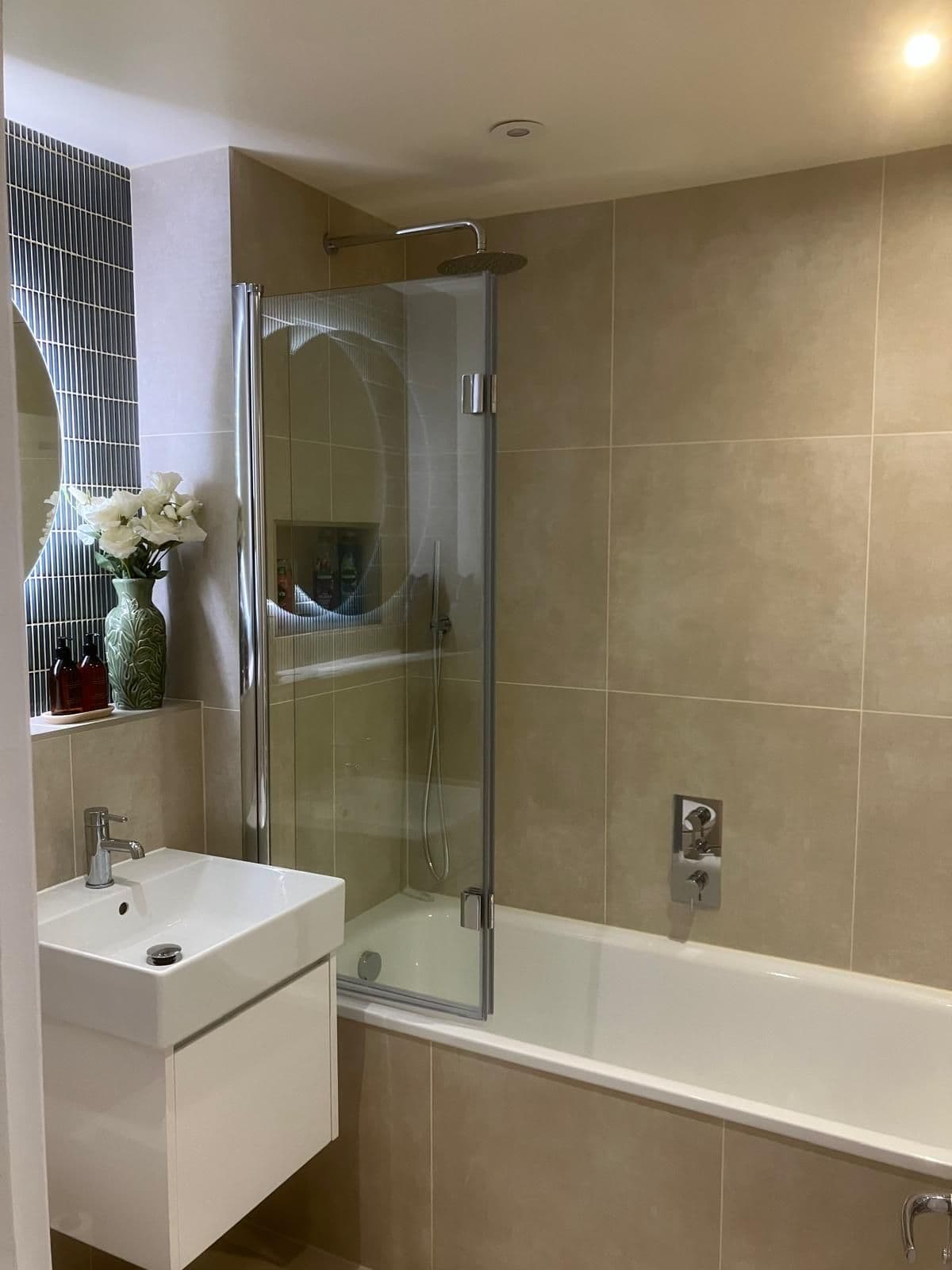 Bath with folding glass shower screen, rainfall head and recessed shower niche, styled with fresh flowers and a blue mosaic feature wall