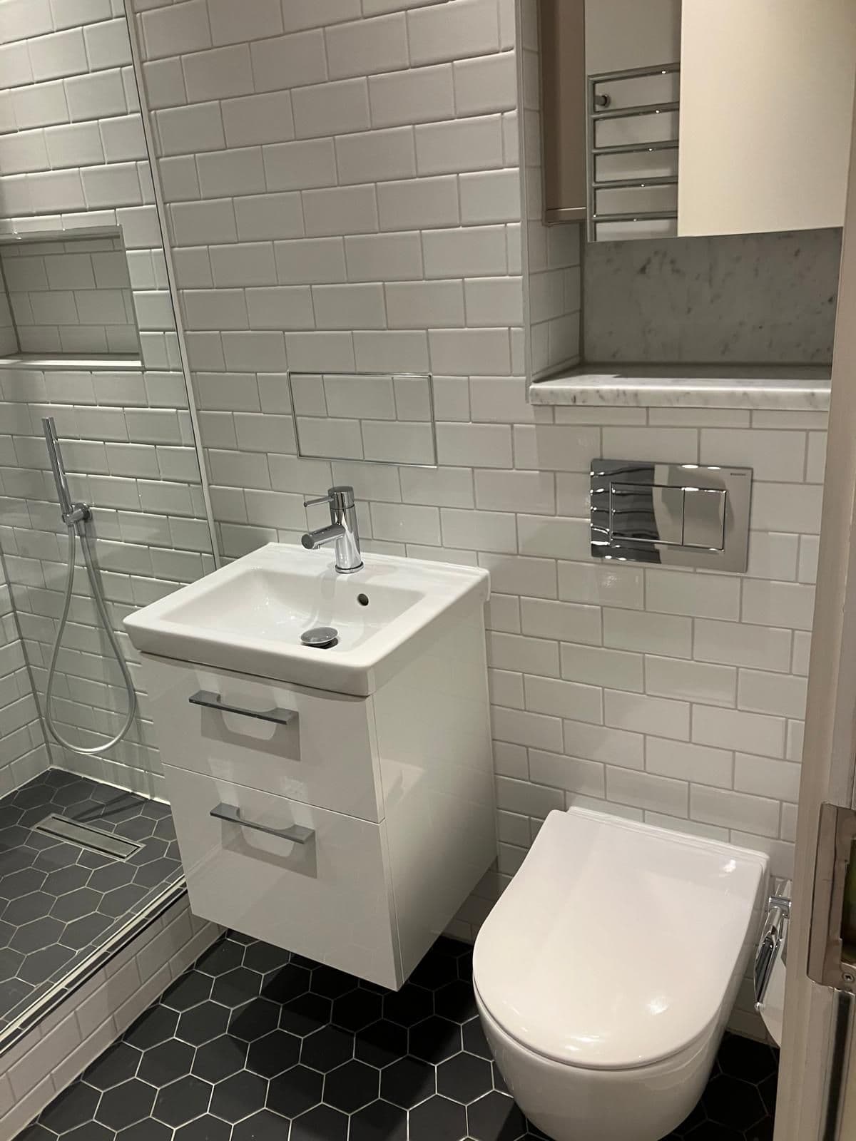 Wall-hung vanity basin beside a concealed-cistern flush plate and toilet, white metro tiling with marble-effect display shelf