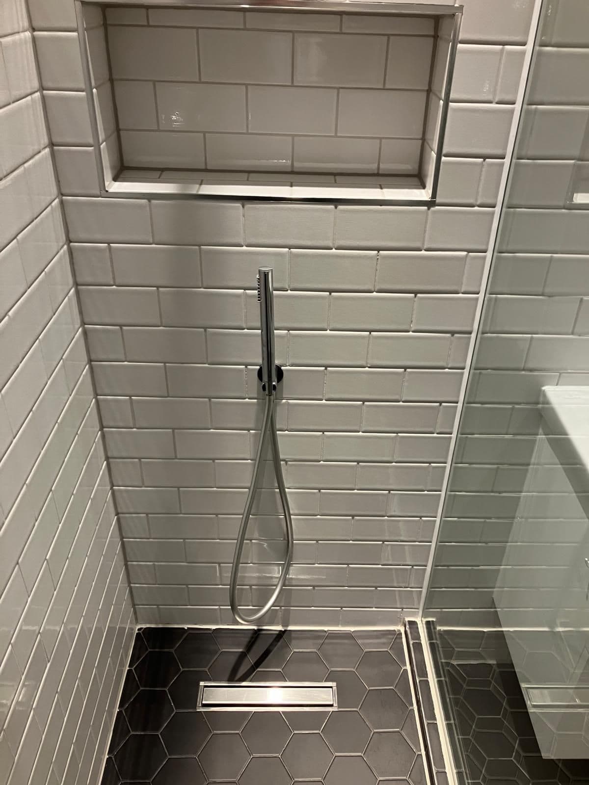 Rainfall shower head over white metro tiling with a recessed storage niche and frameless glass screen