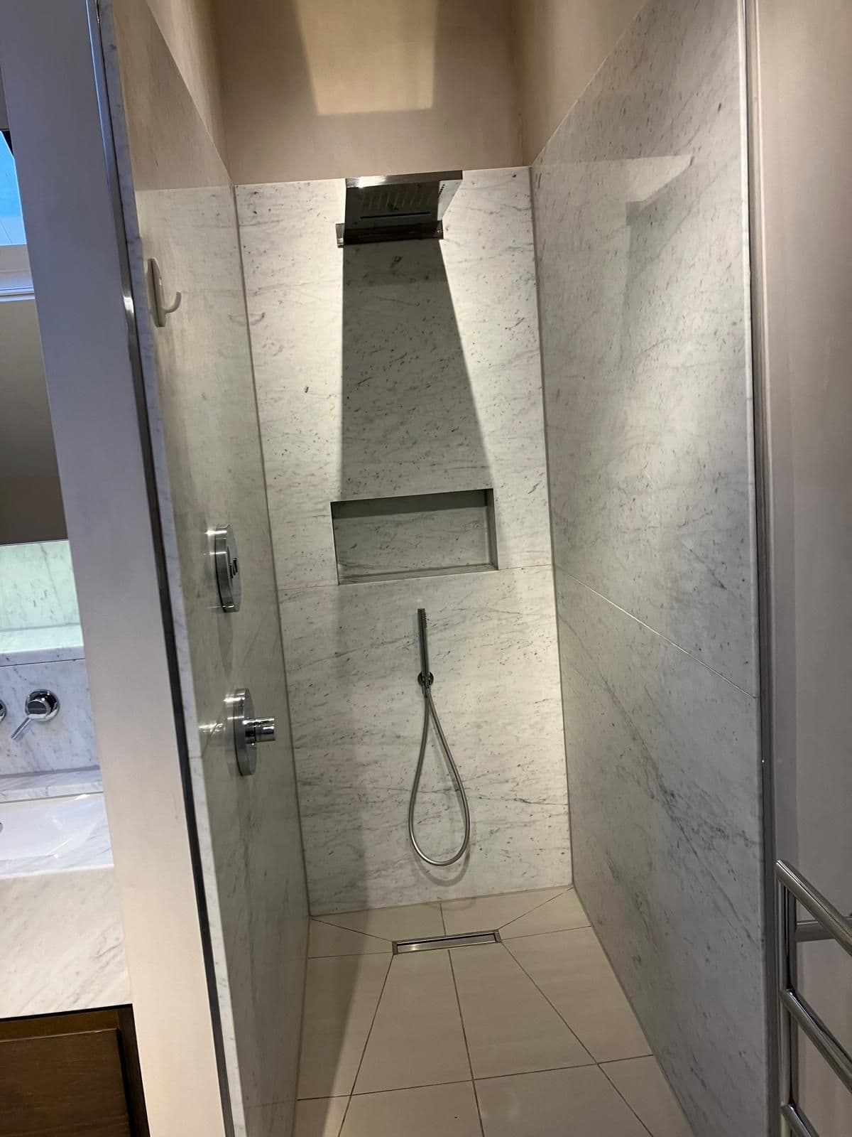 Grey book-matched marble wet-room shower with recessed niche and handheld shower on a riser rail