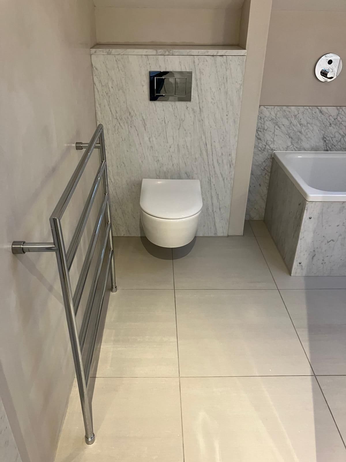Wall-hung toilet against full-height grey marble tiling, chrome heated towel rail and concealed-cistern flush plate
