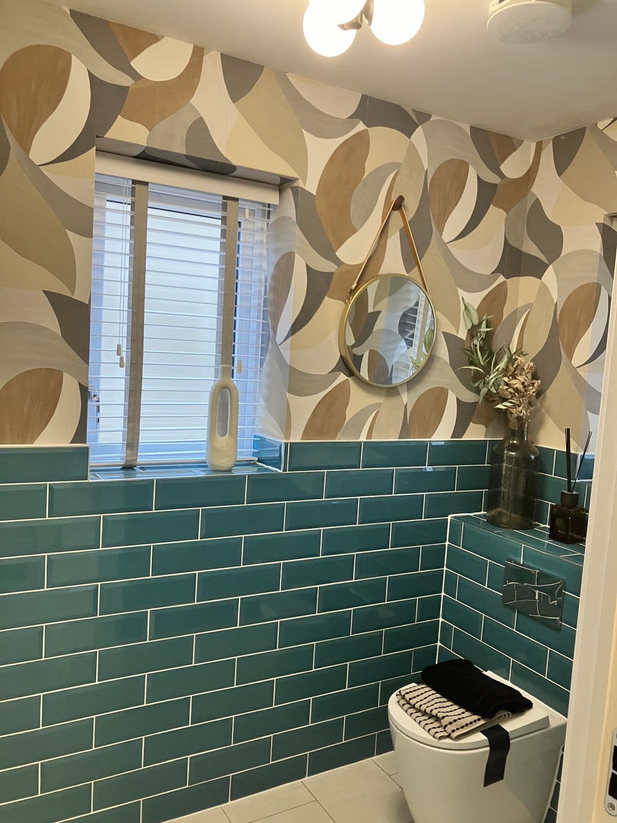 Teal metro-tiled cloakroom with a framed art print, patterned feature wallpaper and white column radiator