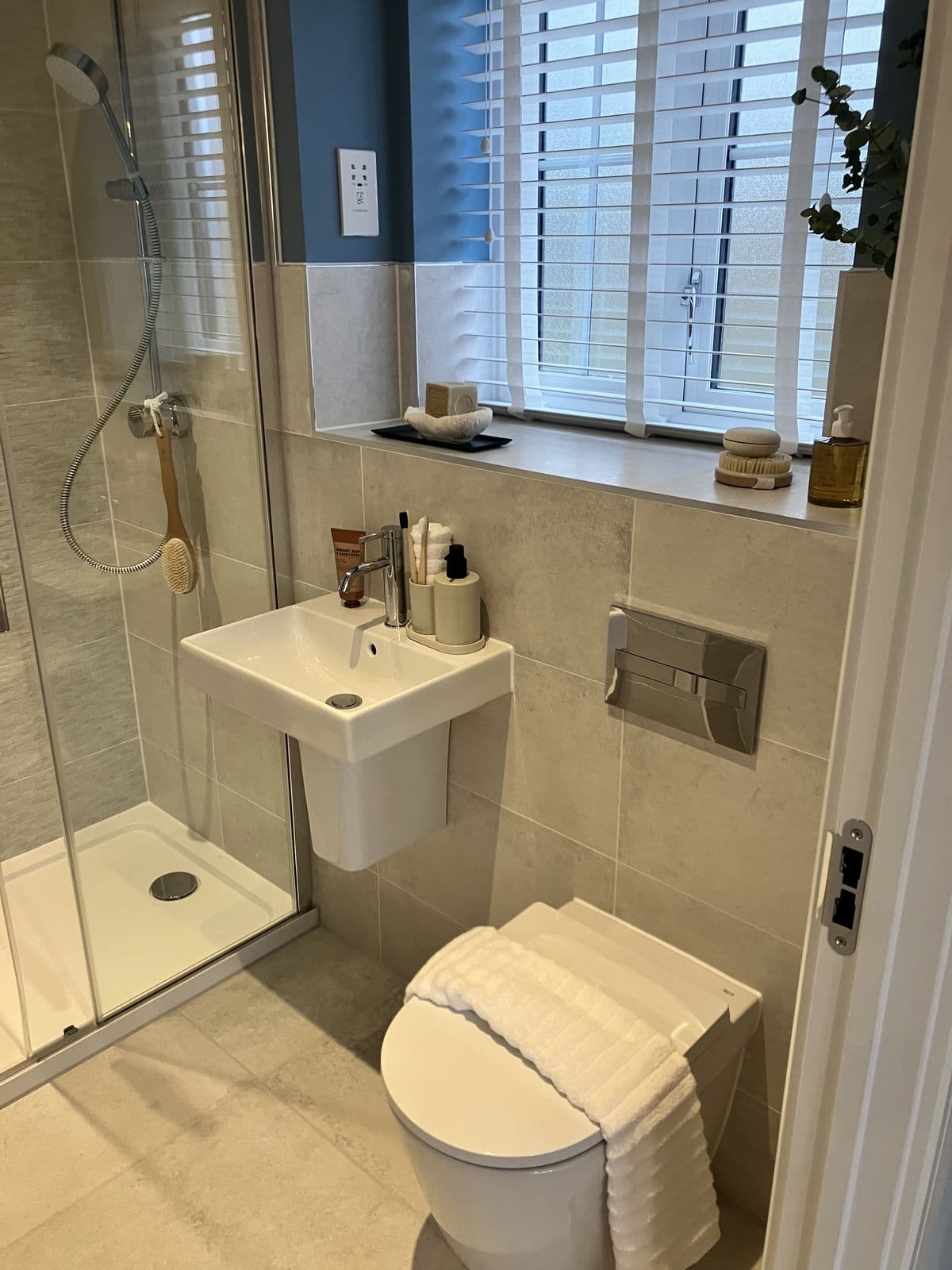 Sliding glass shower door with textured stone-effect tiling and rainfall head, deep blue accent wall and dressed window beyond