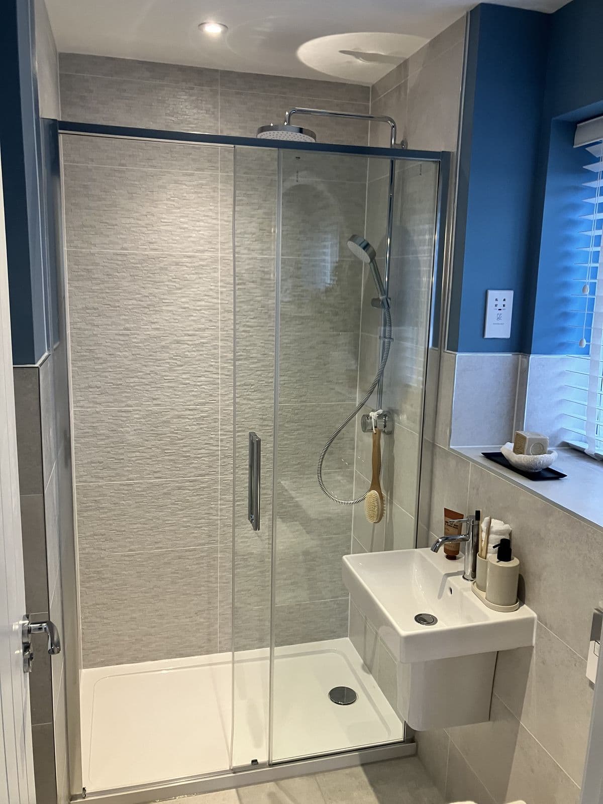 Wall-hung basin with toiletries beneath a windowsill styled with a soap dish and reed diffuser, deep blue accent wall