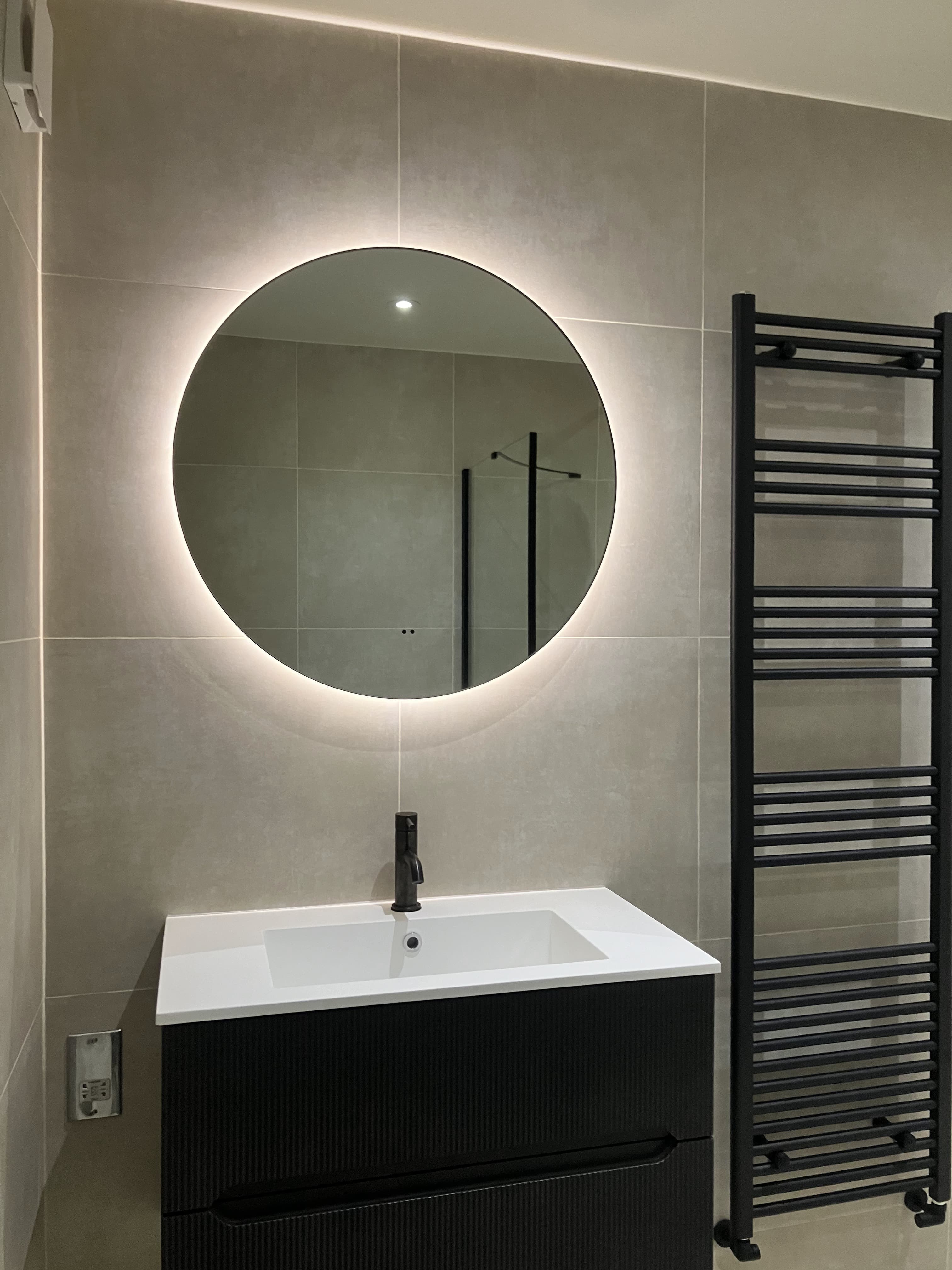 Modern bathroom renovation with illuminated round mirror and black vanity